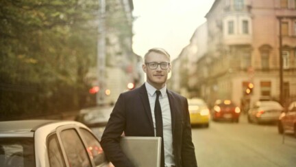 Entschlossener lächelnder Geschäftsmann mit Laptop auf Straße [Quelle: pexels.com]