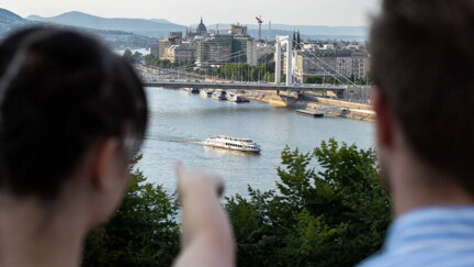 Zwei Menschen stehen auf Hügel und zeigen auf Budapest.