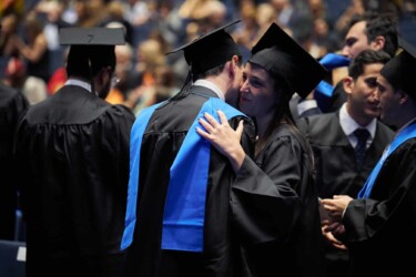 Studierende, gekleidet in der Talar und Graduiertenhut, umarmen sich auf der Exmatrikulationsfeier.