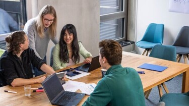 Eine Gruppe Studierender sitzen an einem Tisch und arbeiten.