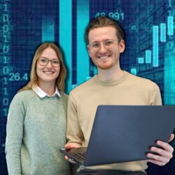 Eine Studentin und ein Student für einer blauen digitalen Wand mit Laptop in der Hand.