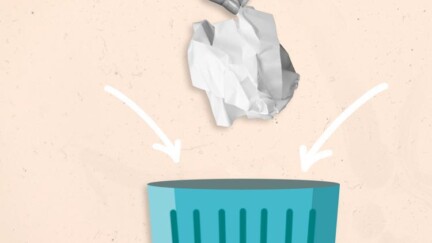 Hand wirft ein zerknülltes Stück Papier in einen Mülleimer, auf dem ein Recycling-Symbol angebracht ist.