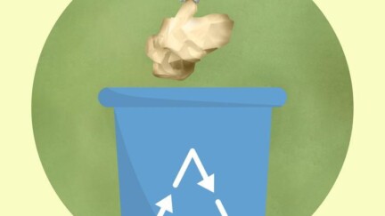 Hand wirft ein zerknülltes Stück Papier in einen Mülleimer, auf dem ein Recycling-Symbol angebracht ist.