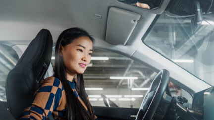 Asiatische Frau sitz in einem Auto und schaut auf ein Display.