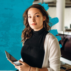Eine Frau mit Tablet in der Hand schaut in die Kamera, hinter ihr ein türkiser Farbklecks und ein Büro.