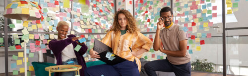 Zwei Frauen und ein Mann kniend in einem Büro, auf der Glaswand hinter ihnen viele bunte Post-Its.