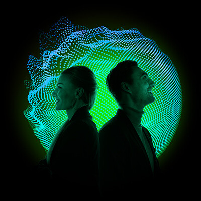Eine Frau und ein Mann stehen mit dem Rücken aneinander gelehnt, der Mann schaut nach rechts oben. Hinter ihnen ein schwarzer Hintergrund, auf dem ein grün leuchtender Kreis mit Wellen steht.