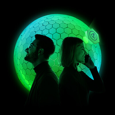 Ein Mann und eine Frau stehen mit dem Rücken aneinander gelehnt, die Frau hält ein Smartphone in der Hand. Hinter ihnen ein schwarzer Hintergrund, davor ein grün-türkis leuchtender Ball.