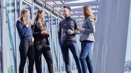 Mehrere junge Menschen in Business-Kleidung stehen auf einem Balkon eines Industriegebäudes