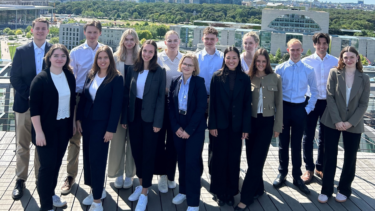 Eine Gruppe junger Menschen in Business-Outfits auf einer Dachterrasse.