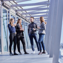 Mehrere junge Menschen in Business-Kleidung stehen auf einem Balkon eines Industriegebäudes