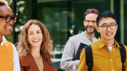 Zwei Frauen und zwei Männer laufen lächelnd vor einem Bürogebäude