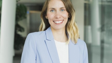 Frau in hellblauem Blazer in einem Flur eines Bürogebäudes.