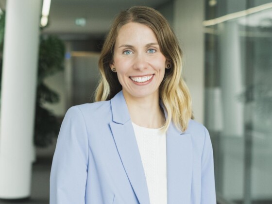 Frau in hellblauem Blazer in einem Flur eines Bürogebäudes.