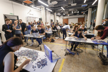 Mehrere Menschen puzzlen an mehreren Tischen.