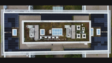 Langgestrecktes Gebäude von oben, Blick auf Flachdach mit Photovoltaik-Modulen.