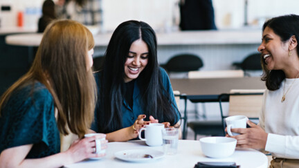 Drei Frauen sitzen am Tisch und sprechen miteinander.