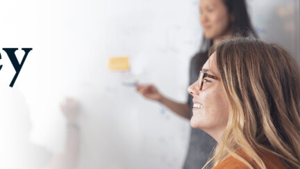 Zwei Frauen vor einem Whiteboard im Hintergrund, eine lächelnd davor