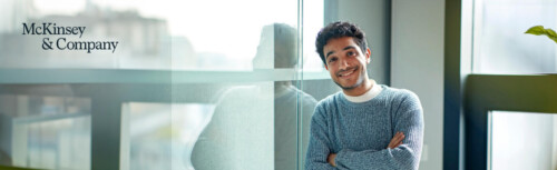 Ein Mann steht mit freundlichem Blick und verschränkten Armen vor einem Fenster am rechten Bildrand, neben ihm links der Slogan McKinsey & Company